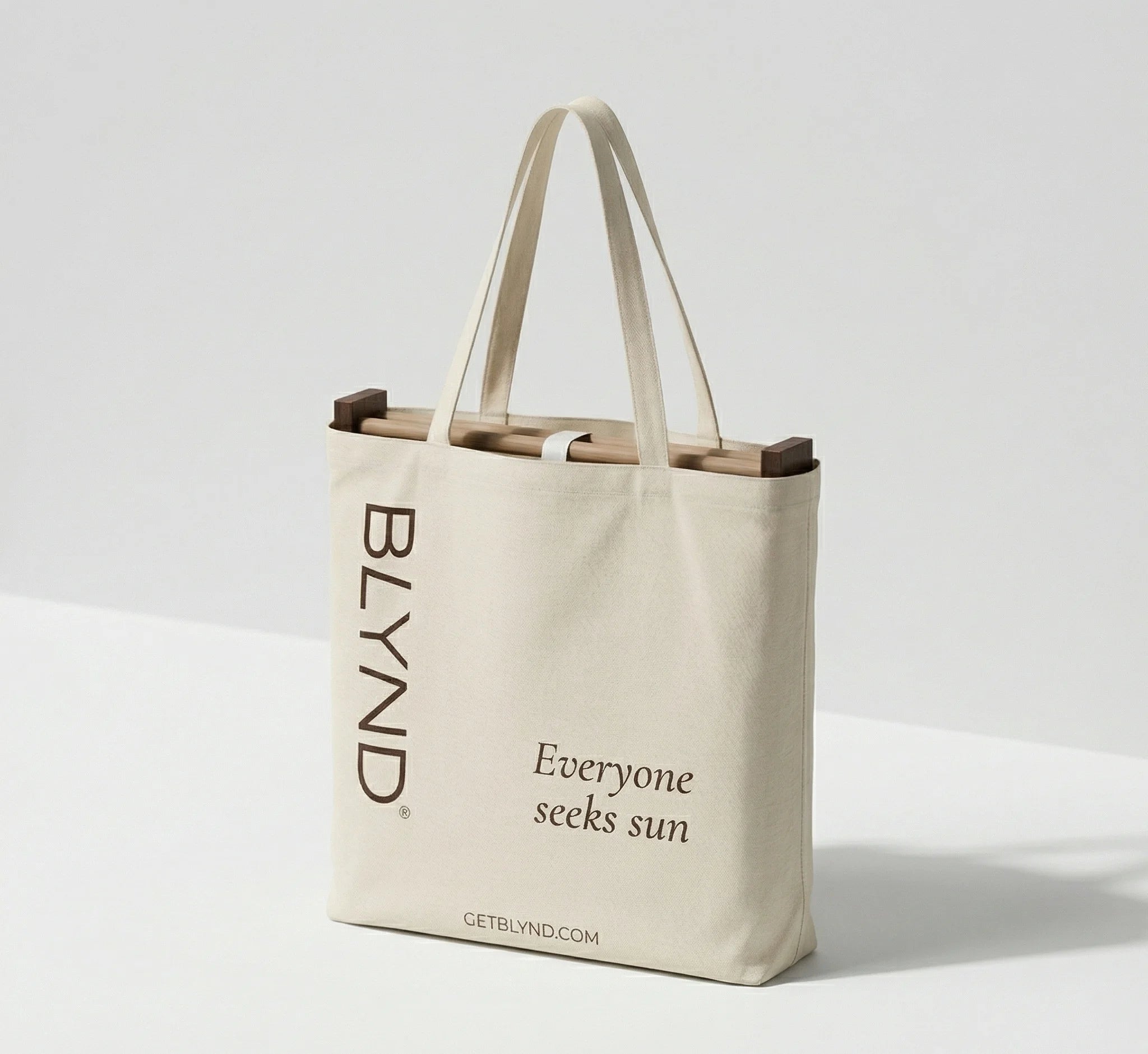 Beige tote bag with folded wooden beach head shade and bottom, featuring BLYND branding and getblynd.com website.